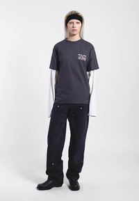 Mörkgrå bomulls t-shirt med vitt logotyp, långa vita ärmar under, kombinerat med mörkblå lösa jeans och svarta vriststövlar.