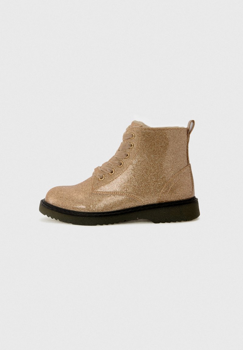 Bottine brillante beige à lacets à l'avant, avec tirant au talon et semelle texturée noire sur un fond clair.