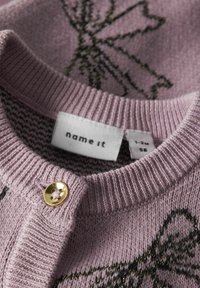 Cárdigan de punto rosa con escote redondo, que presenta patrones de hilo negro y dorado. Detalle de botón dorado con un diseño de flor en la tapeta.