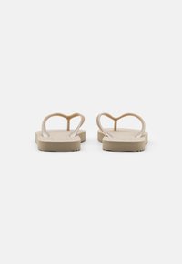 Beige flip-flops with a heart-shaped thong design, made of soft material, featuring a flat sole and textured grip for traction.