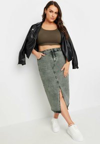 Vihreä oliivinvihreä lyhyt toppi, joka on yhdistetty korkeavyötäröiseen harmaaseen farkkuhameeseen, jossa on etuleikkaus ja kulutettu yksityiskohta. Päällä valkoiset lenkkarit.