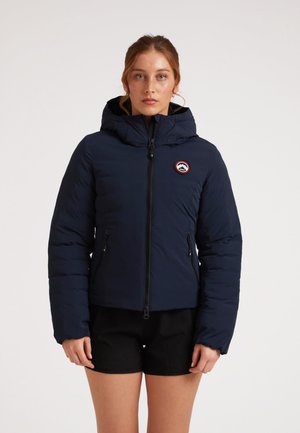 Marineblauwe donsjacket met capuchon, ritssluiting aan de voorkant en twee zijzakken. Heeft een ronde logo op de linkerborst. Gladde textuur.