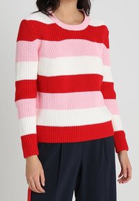 Pull tricoté à rayures rouges, roses et blanches, avec un col rond et des manches longues, doté de poignets et d'un ourlet côtelés.