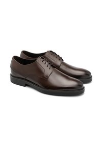 Bruine leren schoenen met een strak ontwerp, ronde neus, veters en een lage zwarte rubberen zool. Gladde textuur en minimale accenten.