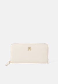Portafoglio in pelle beige con logo dorato, forma rettangolare, texture liscia e chiusura con zip. Presenta un sottile tirante per la zip a un'estremità.