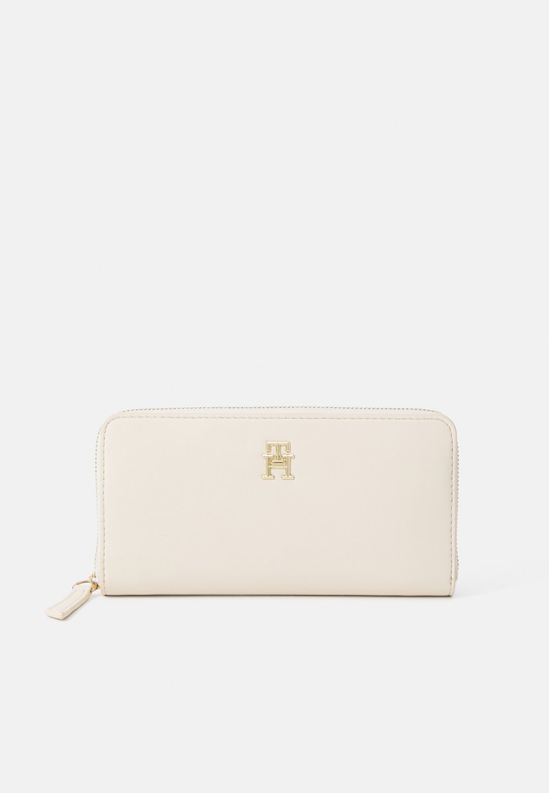 Beige leather wallet with a gold logo, rectangular shape, smooth texture, and zip closure. Features a thin zipper pull at one end.