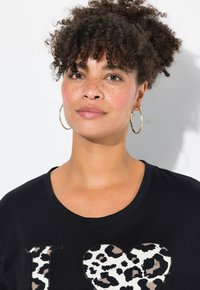 T-shirt noir avec un design de cœur imprimé léopard blanc. Le col est rond, avec une texture lisse et une coupe décontractée.