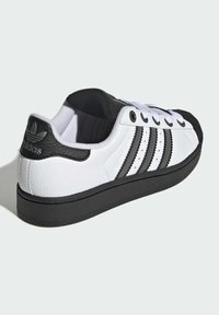 Biele tenisky s čiernymi akcentmi, s textúrovaným koženým zvrškom, tromi čiernymi pruhmi a čiernou gumovou podošvou.