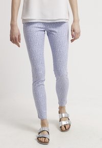 Leggings de color azul claro con un estampado floral y un diseño ajustado, fabricados con una tela elástica. Combinados con sandalias de hebilla plateada para un look casual.