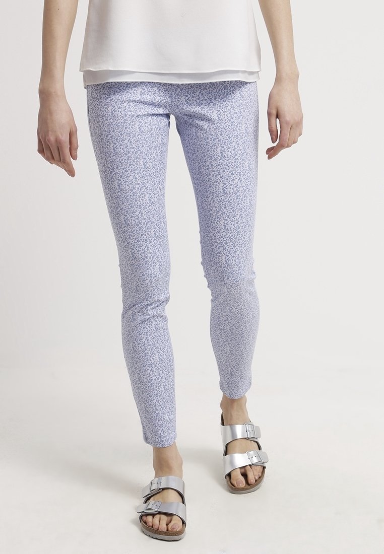 Leggings de color azul claro con un estampado floral y un diseño ajustado, fabricados con una tela elástica. Combinados con sandalias de hebilla plateada para un look casual.