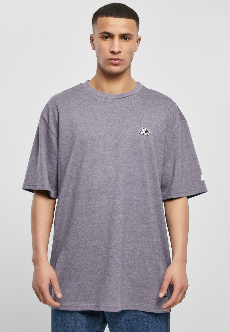Purple cotton t-shirt with a relaxed fit, short sleeves, round neckline, and a small logo on the chest. Paired with blue jeans.