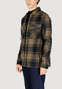 Camicia in flanella con un motivo scozzese verde e nero, maniche lunghe, due tasche sul petto e un design con bottoni sul davanti.