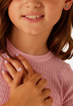 Lachend kind met bruin haar tot op de schouders, draagt oorbellen in de vorm van een hartje en een roze trui met textuur, handen gekruist over de borst.