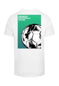 Balta T-krekls ar grafisko dizainu, kas attēlo futbolu un uzrakstu "SUNDAY FOOTBALL CLUB" uz zaļa fona biezajās burtnēs.