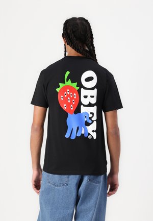 Juodas medvilnės marškinėliai su dideliu raudonos braškės grafiku, turinčia akis ir mėlyną ranką, šalia žodžio "OBEY" balta spalva.