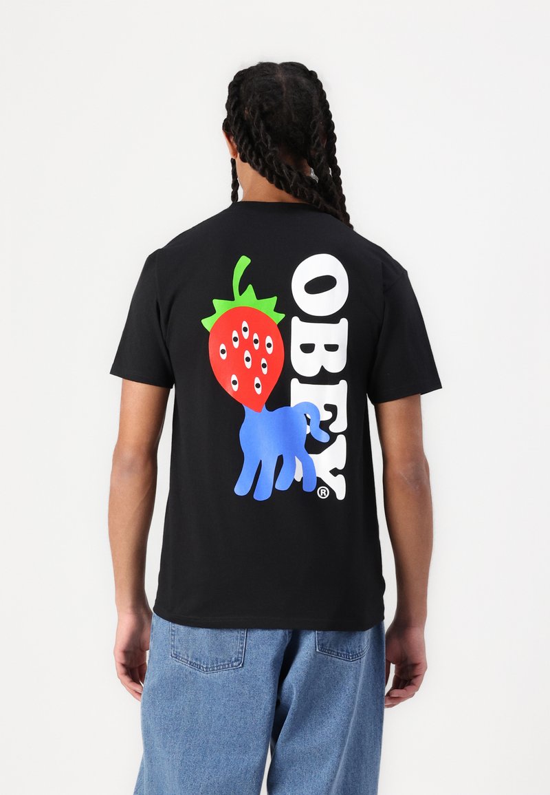 Fekete pamut póló, amelyen egy nagy grafika látható: egy piros eper szemekkel és egy kék kéz, mellette pedig az "OBEY" felirat fehér színben.
