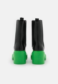 Czarne skórzane botki za kostkę o gładkim wykończeniu z zielonymi, masywnymi obcasami w kształcie bloku, z tylnymi uchwytami ułatwiającymi zakładanie.