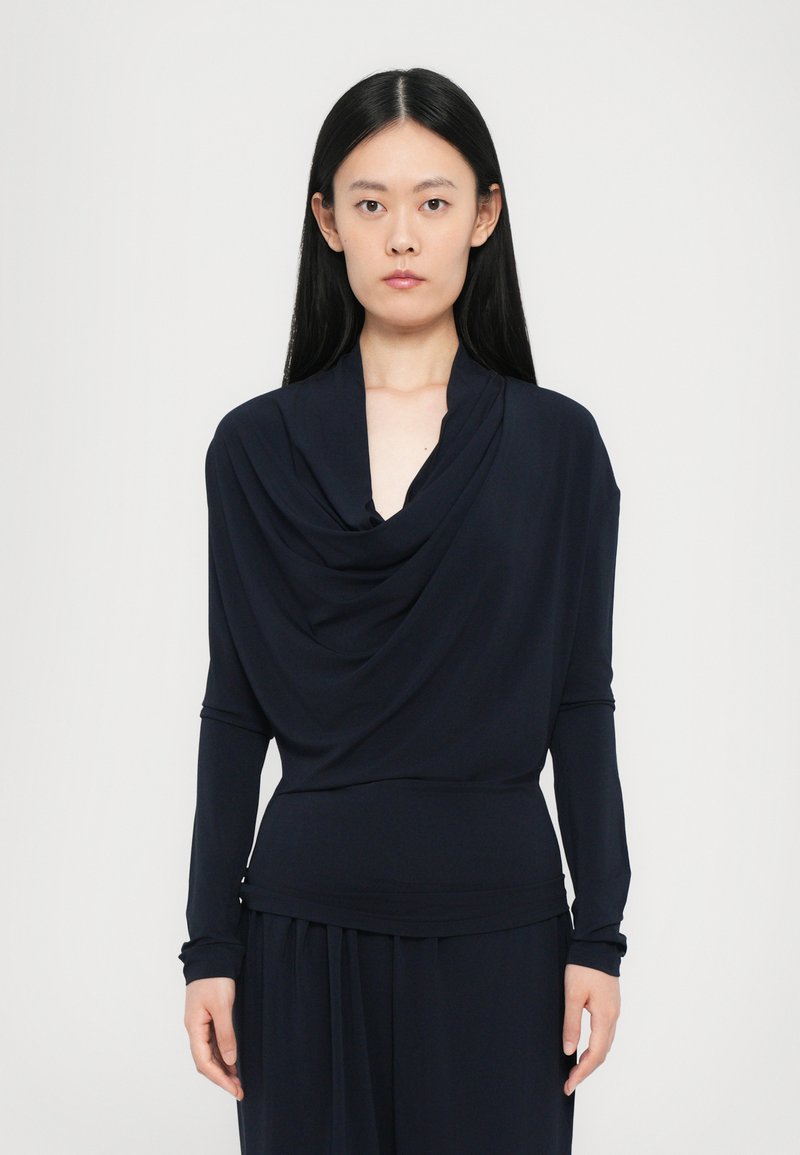Navy draped long-sleeve top with a cowl neckline, smooth texture, and close-fitting silhouette, paired with matching bottoms.