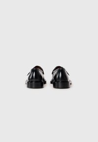 Un par de zapatos de vestir de cuero negro pulido vistos desde atrás sobre un fondo blanco plano.