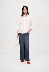 White button-up shirt with eyelet pattern, long denim skirt with front slit, red high-heeled shoes, and a white handbag.