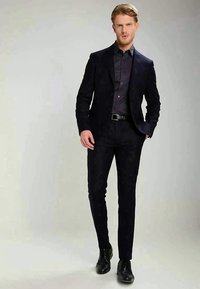 Navy suit with a fitted blazer and matching trousers, paired with a dark button-up shirt and polished black shoes. Smooth fabric, tailored design.