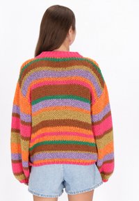 Oversized, dzianinowy sweter z wielokolorowymi paskami w odcieniach pomarańczowym, różowym, fioletowym, brązowym i zielonym. Posiada opadające ramiona i okrągły dekolt.
