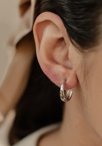 Silberne Ohrringe in Form von Ringen, runde Form mit polierter Oberfläche, hängend vom Ohrläppchen, sichtbare Textur mit leichten Designelementen.