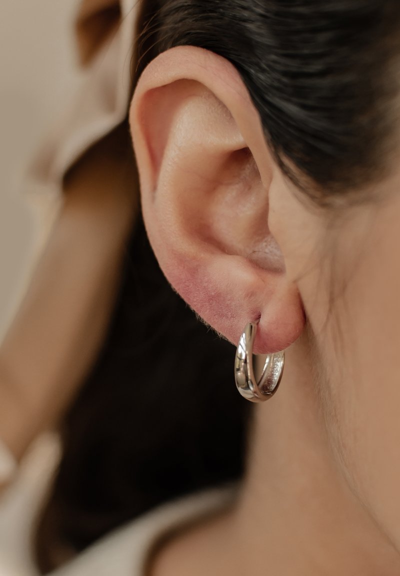 Silberne Ohrringe in Form von Ringen, runde Form mit polierter Oberfläche, hängend vom Ohrläppchen, sichtbare Textur mit leichten Designelementen.