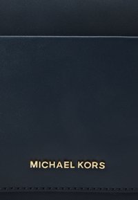 Granatowa torba materiałowa z złotym logo "MICHAEL KORS", charakteryzująca się teksturowanym wykończeniem i prostymi liniami, oferująca elegancki i nowoczesny design.