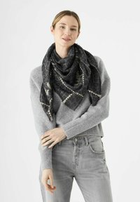 Sciarpa con stampa animale nera e beige con bordi frangiati, drappeggiata attorno al collo, abbinata a un maglione grigio chiaro e jeans.