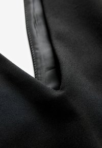 Gros plan d’un tissu noir avec un col en V montrant une texture lisse et une couture fine le long du bord.