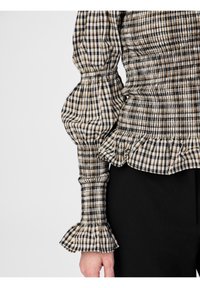 Checkered beige, black, and white long-sleeve blouse with ruched fabric, puffed sleeves, ruffled cuffs, and black pants.