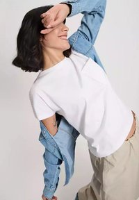 Biała koszulka z krótkim rękawem z kieszonką, noszona pod jasnoniebieską koszulą dżinsową, zestawiona z luźnymi, beżowymi spodniami.