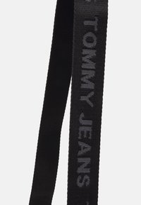 Svart tygbälte med vävd struktur och präglad "TOMMY JEANS"-logotyp i grått. Bältet har en ren, minimalistisk design.