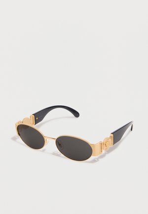 Gafas de sol ovaladas con lentes negras, montura de metal dorado y varillas negras con detalles decorativos circulares dorados.