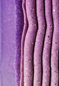 Sei rotoli di tessuto in diverse sfumature di viola, con una finitura texture e paillettes metalliche dorate e argentate sparse.