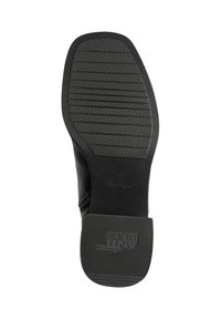 Semelle de chaussure noire avec un motif texturé, présentant des rainures horizontales et une marque. Fabriquée en caoutchouc, la semelle a un design plat et des bords arrondis.