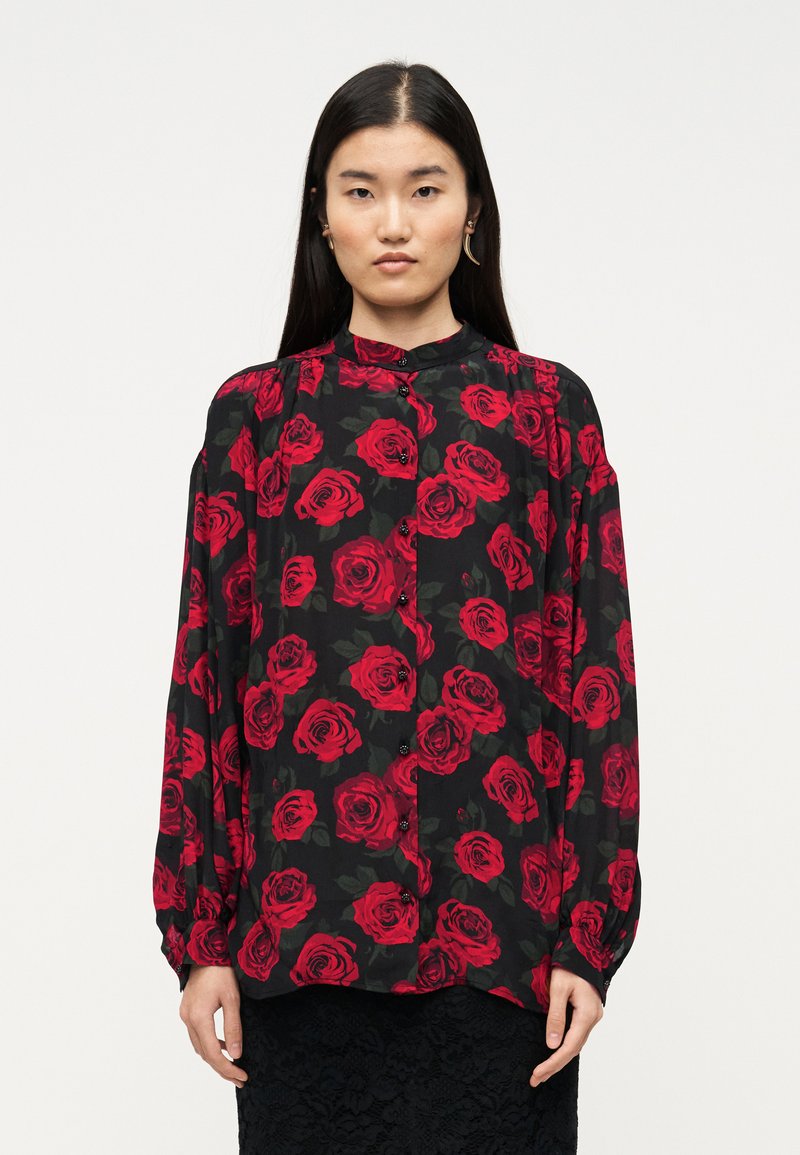 Μαύρο μπλουζάκι με κόκκινα σχέδια τριαντάφυλλων, μακριά μανίκια, κούμπωμα με κουμπιά μπροστά και ψηλό λαιμόκομμα. Κατασκευασμένο από ελαφρύ ύφασμα.