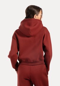 Felpa bordeaux con un ampio cappuccio, texture morbida e polsini a coste. Il design presenta una vestibilità rilassata e una vita.