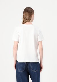 Witte katoenen t-shirt met een ronde halslijn en korte mouwen, gecombineerd met hoog getailleerde blauwe spijkerbroek. Eenvoudig, casual ontwerp.