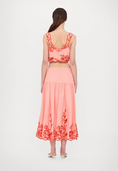 Zweiteiliges Outfit bestehend aus einem cropped Top und einem langen Rock. Der Stoff ist pink mit kontrastierenden roten Blumenstickereien entlang der Kanten.