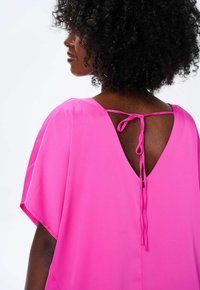Fuksjowa sukienka o luźnym kroju i krótkich rękawach. Posiada głęboki dekolt w serek z zapięciem na kokardę. Gładki, lekki materiał.