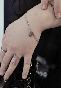 Silberne Kettenarmband mit einem herzförmigen Anhänger, der ein Sonnenmuster zeigt. Hand verziert mit einem silbernen ringslangförmigen Ring und einem Perlenring.