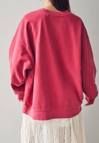 Felpa rossa oversize con scollatura rotonda, spalle cadenti e maniche a costine. Tessuto morbido e testurizzato con una vestibilità comoda.