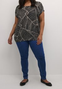 Haut à manches courtes noir et crème à motif, avec une coupe ample, associé à un jean skinny bleu et des ballerines noires.