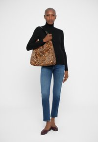 Borsa hobo in fabric leopardato, con tracolla, caratterizzata da una forma oversize e una texture liscia. Indossata da una persona in jeans e una maglietta nera.