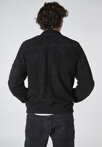 Svart mockabomberjacka med ribbade muddar och nederkant; har en slät yta och en minimalistisk design utan synlig branding.