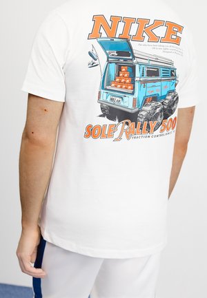 T-shirt blanc avec texte orange "NIKE", illustration d'une camionnette tout-terrain bleue chargée de boîtes à chaussures, et "SOLE RALLY 500" en orange en dessous.