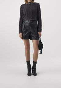Maglione viola a costine con maniche lunghe, abbinato a pantaloni corti in pelle nera e stivaletti neri alla caviglia. Tiene una piccola borsa nera texturizzata.
