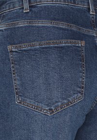 Mörkblå denimjeans med en klassisk fem-fickdesign, som har en enda bakficka med orange sömmar och en slät yta.